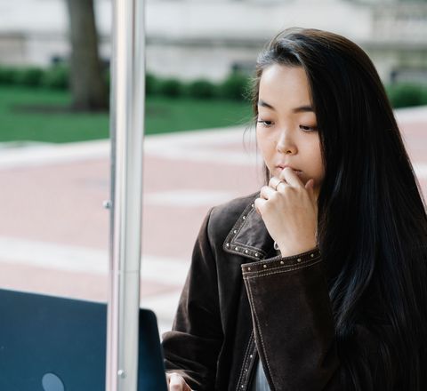 A recent graduate studying on a laptop outside a campus building